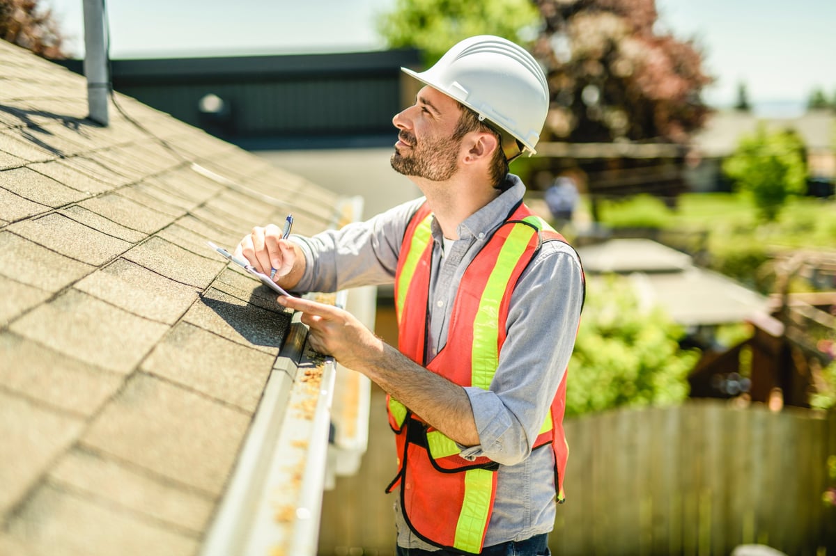 Ironcrest Exteriors website project — a roofing contractor with a white hard hat and clipboard inspecting a home, example of storm-damage assessment work